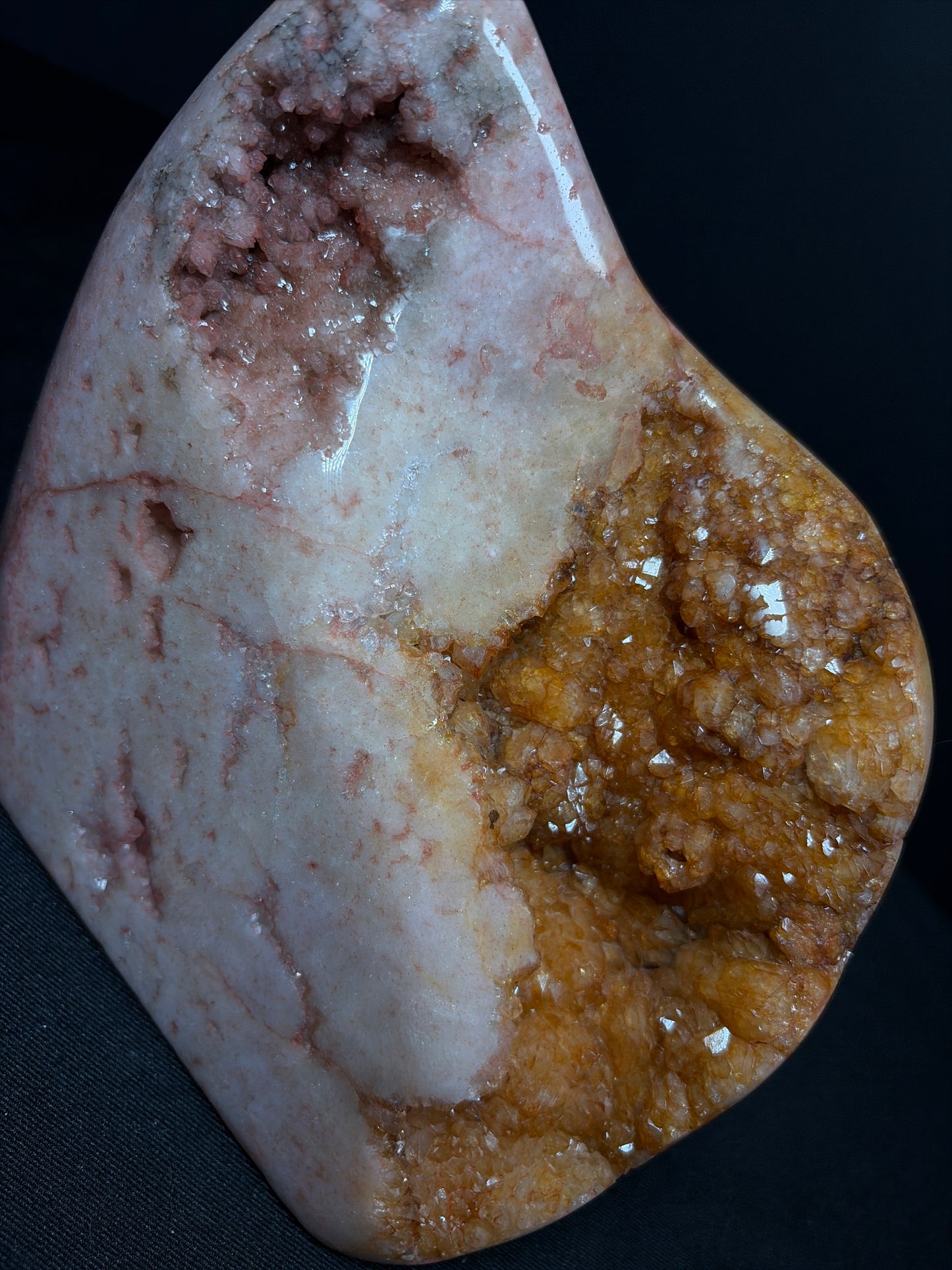 Close-up of a polished pink amethyst and citrine freeform crystal against a dark background. The stone shows soft blush-pink and creamy white tones with subtle natural veining, a sparkling pink amethyst druzy pocket near the upper left, and a dense honey-gold citrine crystal cluster covering the right side, creating a striking contrast of textures and colors.