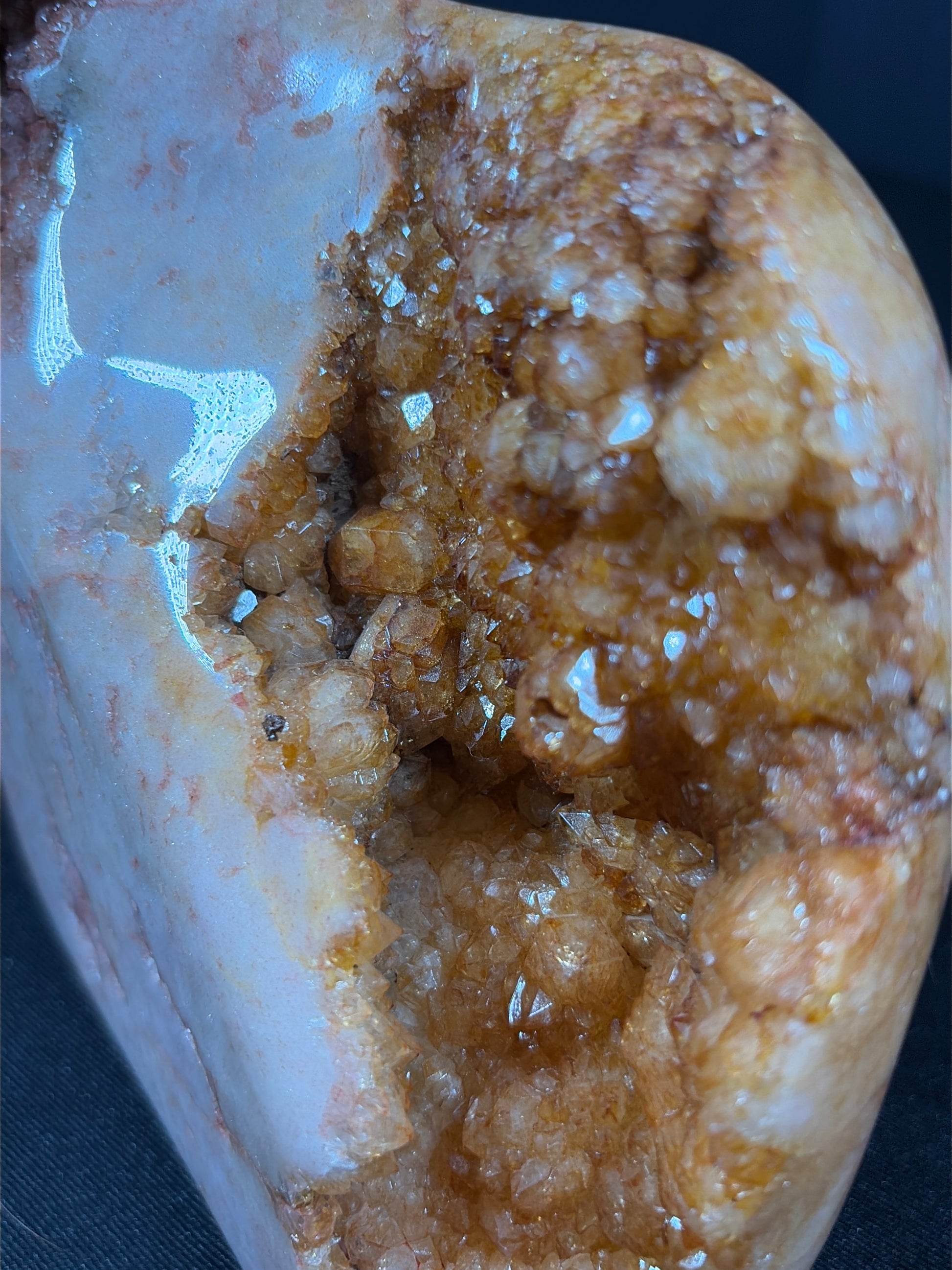 Close-up view of a polished pink amethyst and citrine freeform crystal showing a deep natural cavity filled with sparkling honey-gold citrine crystals. The surrounding stone displays smooth blush-pink and creamy white tones with glossy polish, creating a contrast between the rough crystal interior and the polished outer surface.